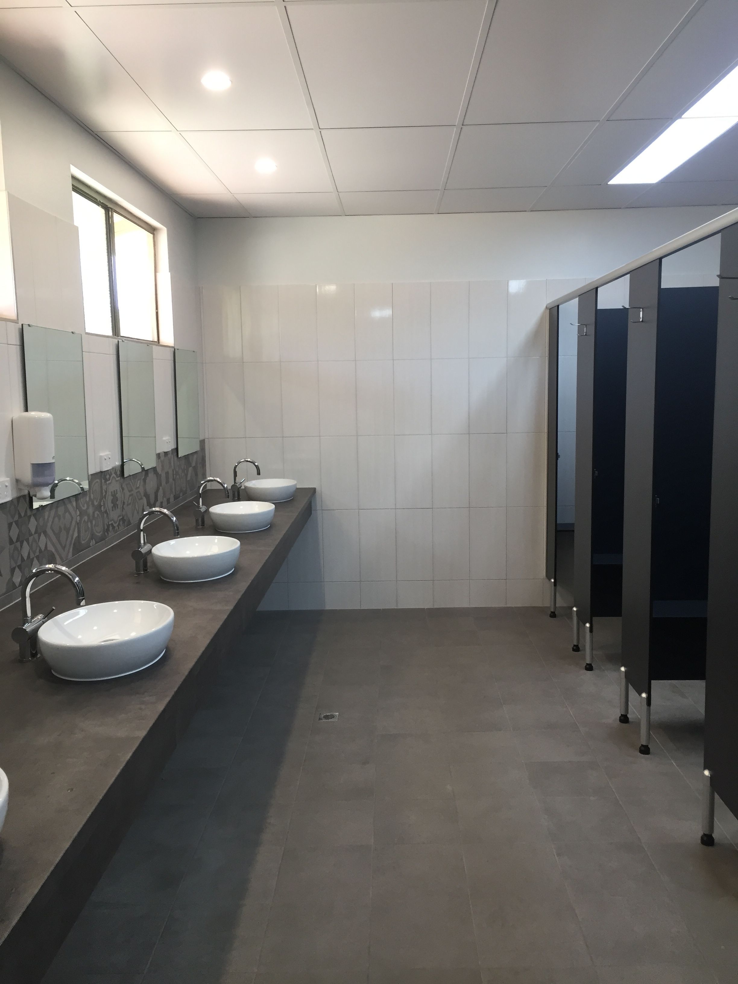 Uma casa de banho moderna com três lavatórios, um secador de mãos e um espelho.