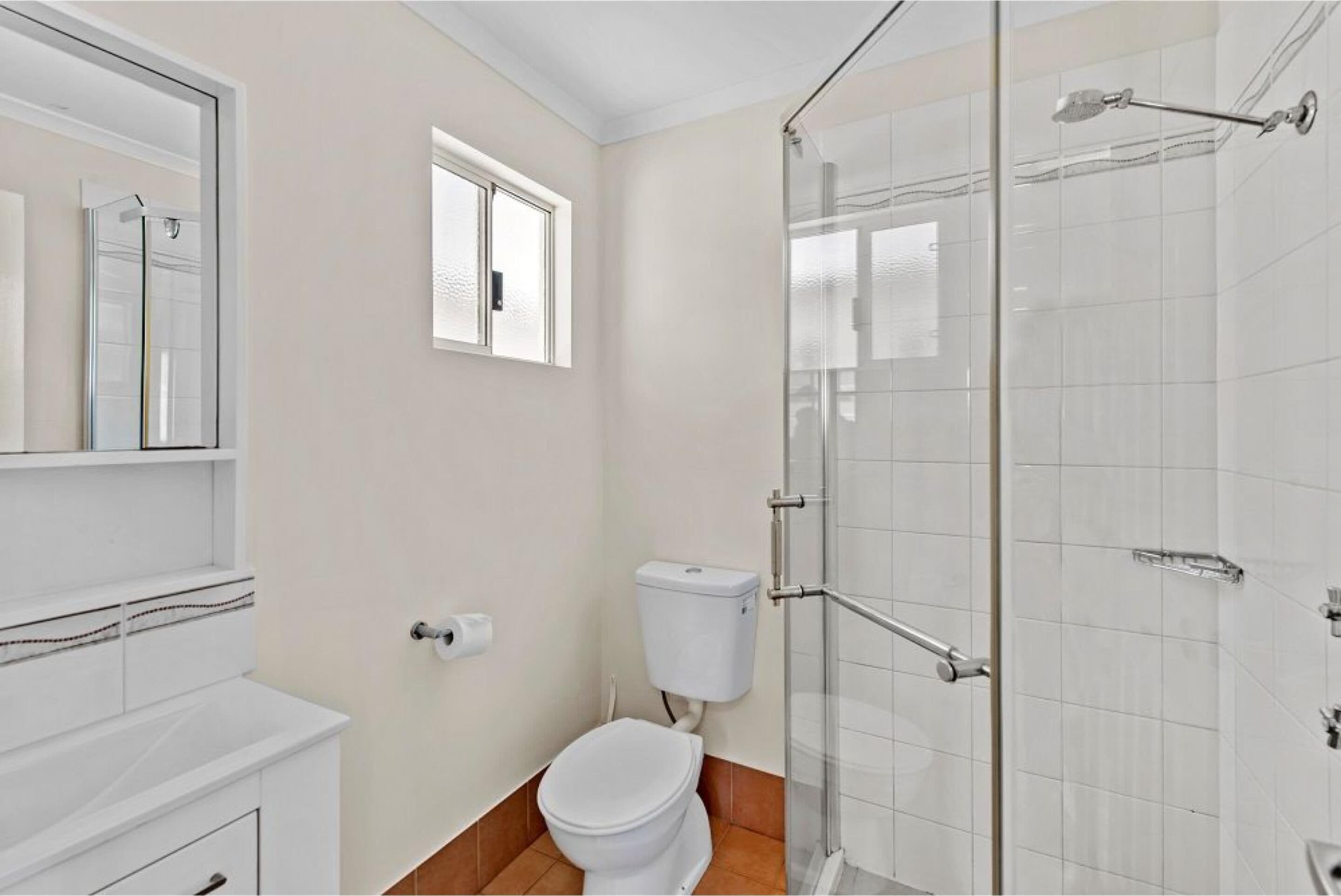 Un baño con inodoro, ducha con mampara de vidrio y espejo sobre el lavabo.
