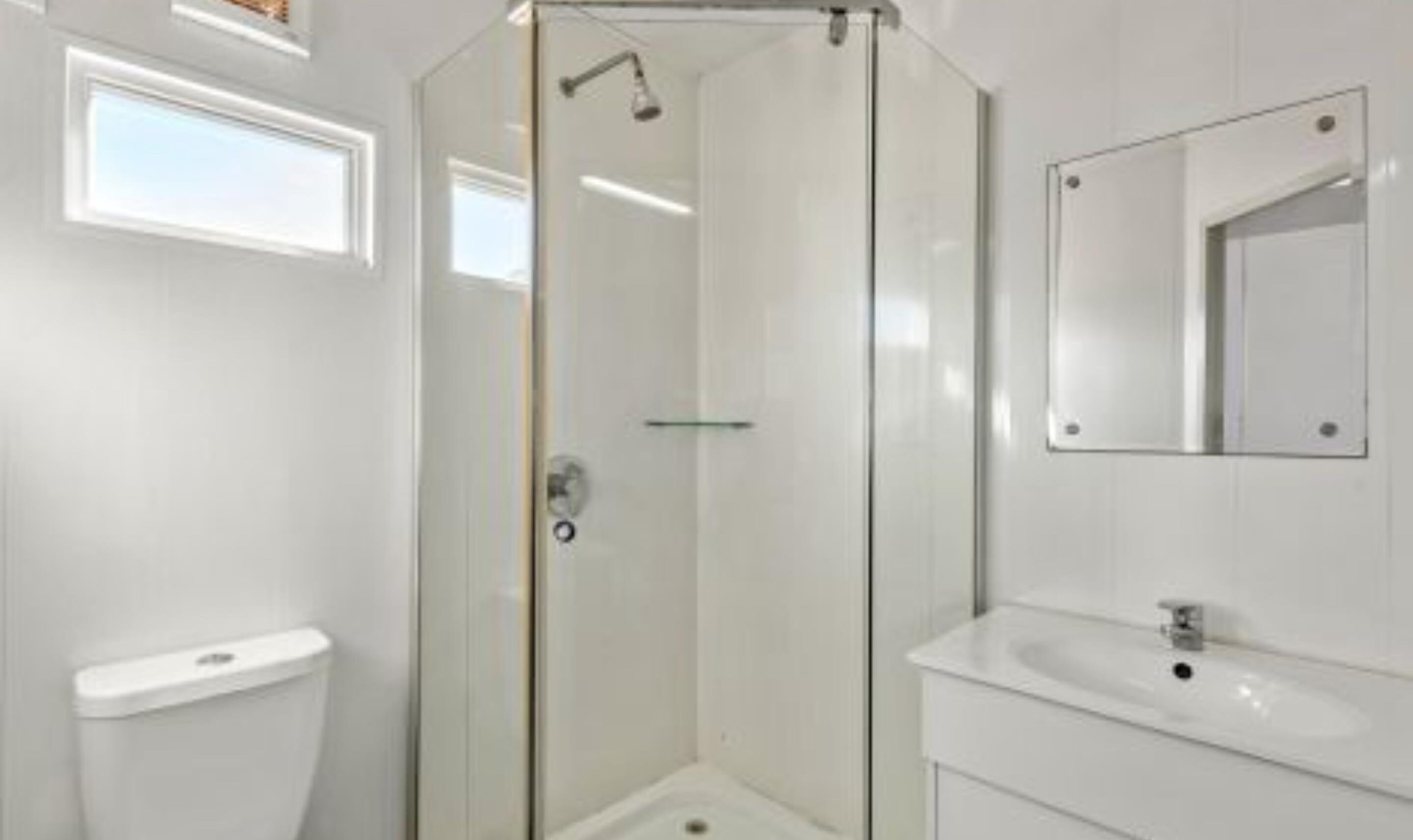 A modern bathroom with a glass-enclosed shower, a white toilet, and a sink with a mirror.