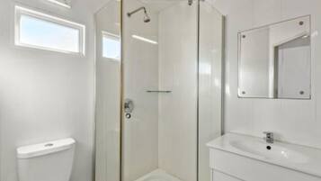 A modern bathroom with a glass-enclosed shower, a white toilet, and a sink with a mirror.