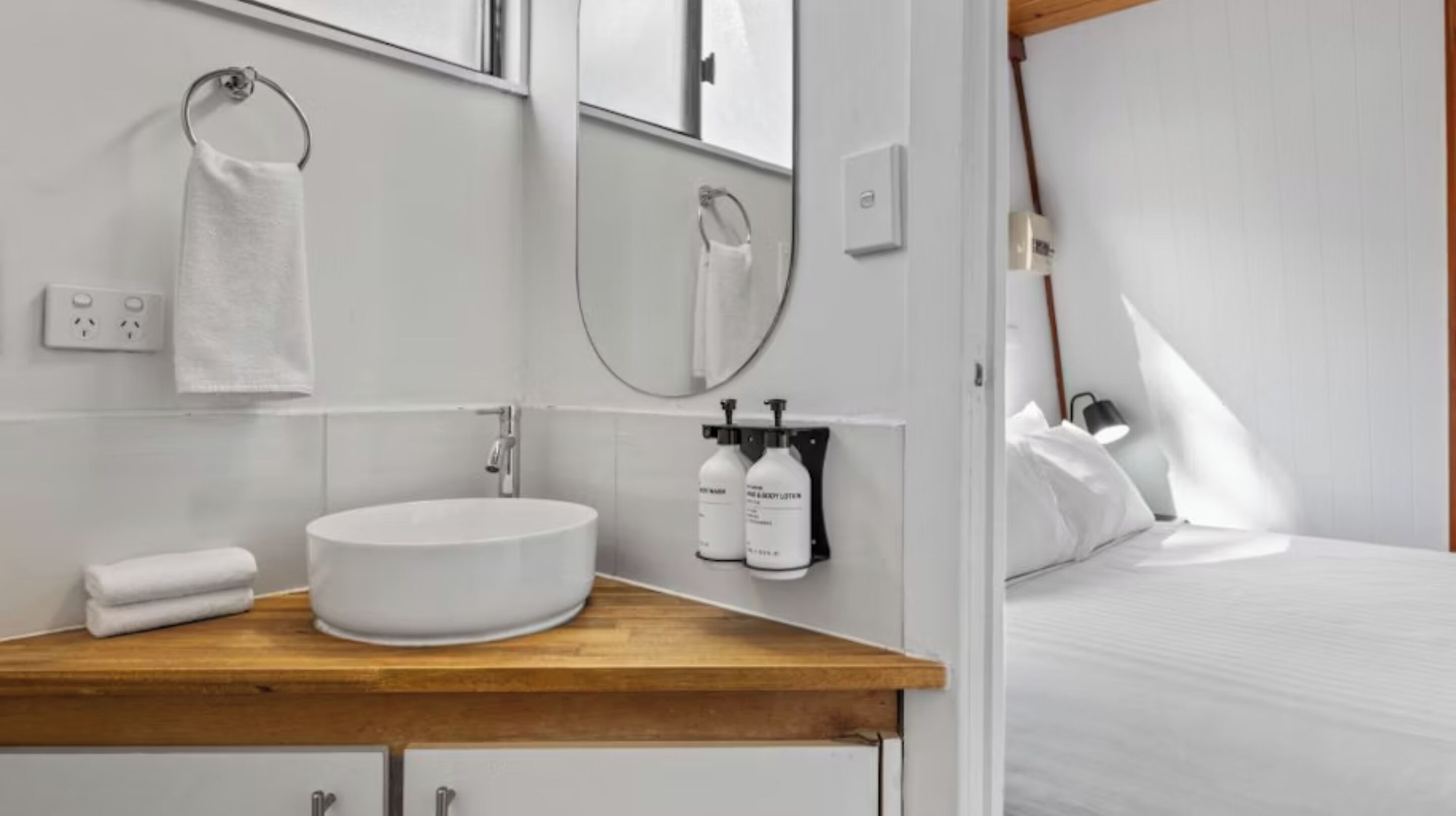 A modern bathroom with a wooden vanity, a round sink, a mirror, and two bottles of body lotion.