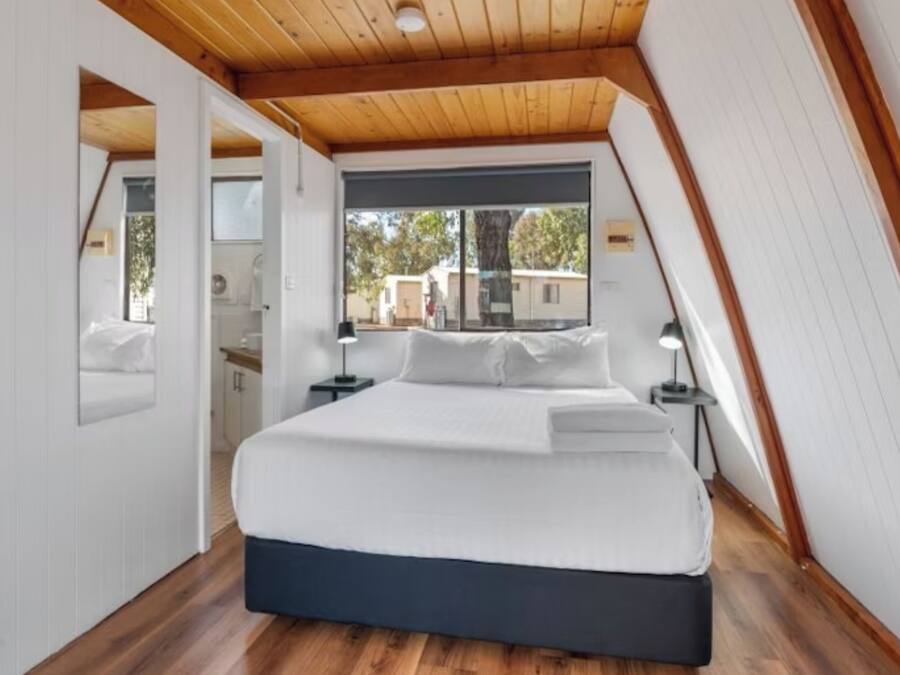 A bedroom with a bed, wooden ceiling, and a window.