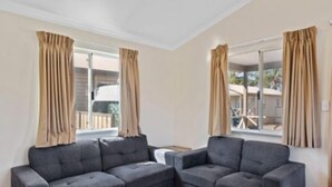 A modern living room with a grey sectional sofa, beige curtains, and a view of a balcony. - Discovery Parks - Kalgoorlie Goldfields (Boulder)