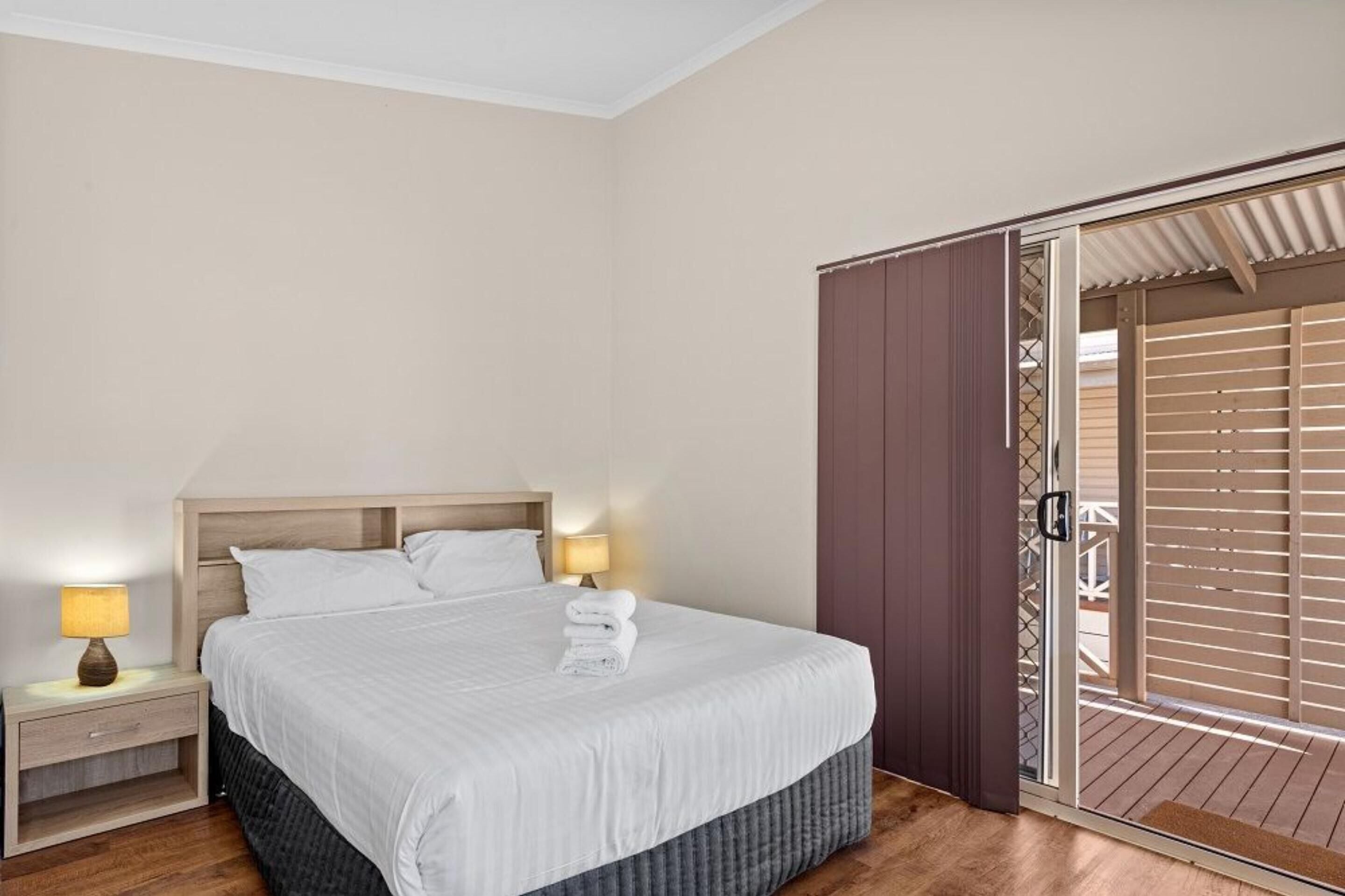 A hotel room with a bed, nightstands, a lamp, and a sliding door to a balcony.