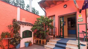 A hotel entrance with a red exterior, a small porch with steps, and potted plants. - Hotel Greco (Milan)