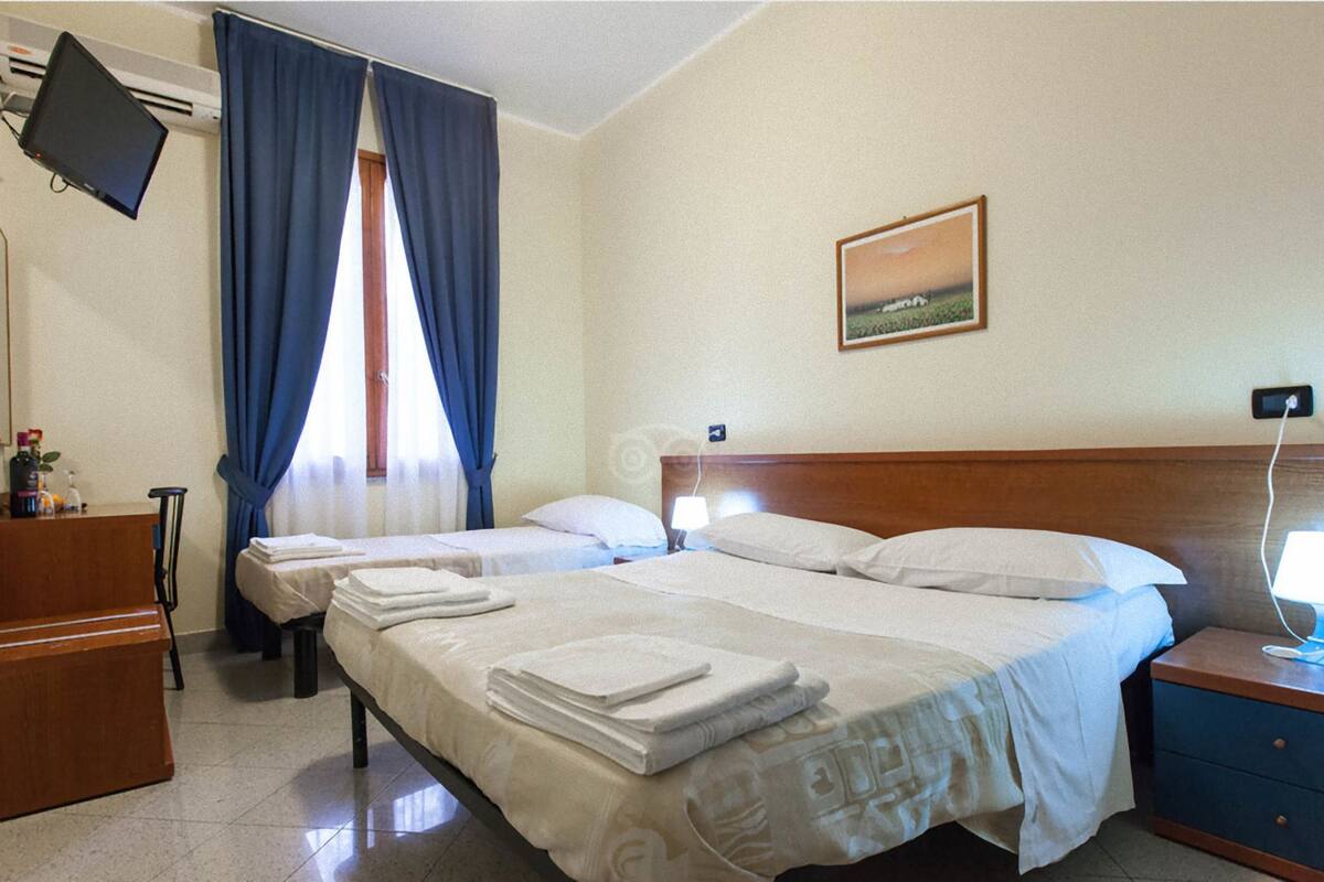 Een hotelkamer met twee bedden, een bureau, een televisie en een schilderij aan de muur.