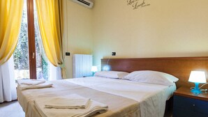 A hotel room with a bed, a nightstand, a lamp, and a window with curtains. - Hotel Greco (Milan)