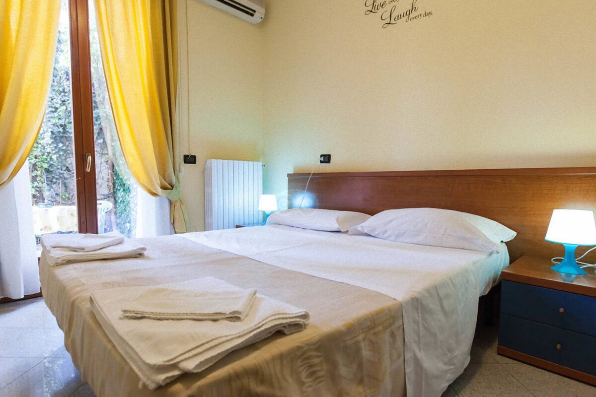 Een hotelkamer met een bed, nachtkastje, lamp en een raam met gordijnen.