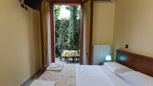 A hotel room with two beds, a table with chairs, and a view of a garden through an open door. - Hotel Greco (Milan)