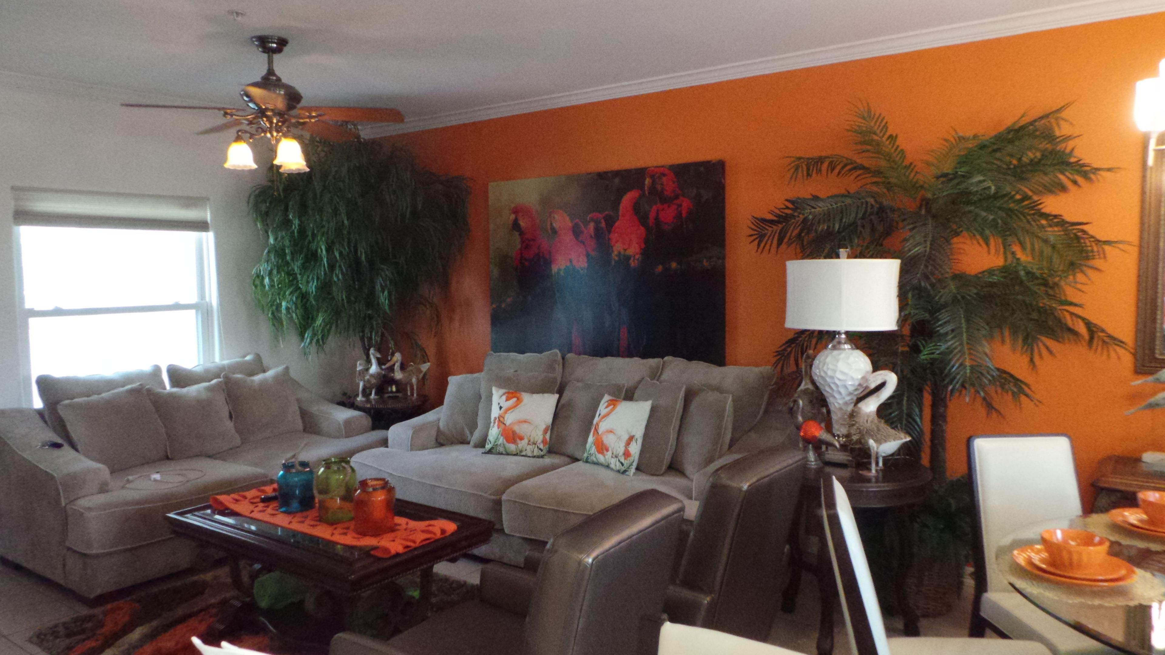 A living room with a sofa, coffee table, and decorative items. There is a ceiling fan, a painting on the wall, and a lamp.