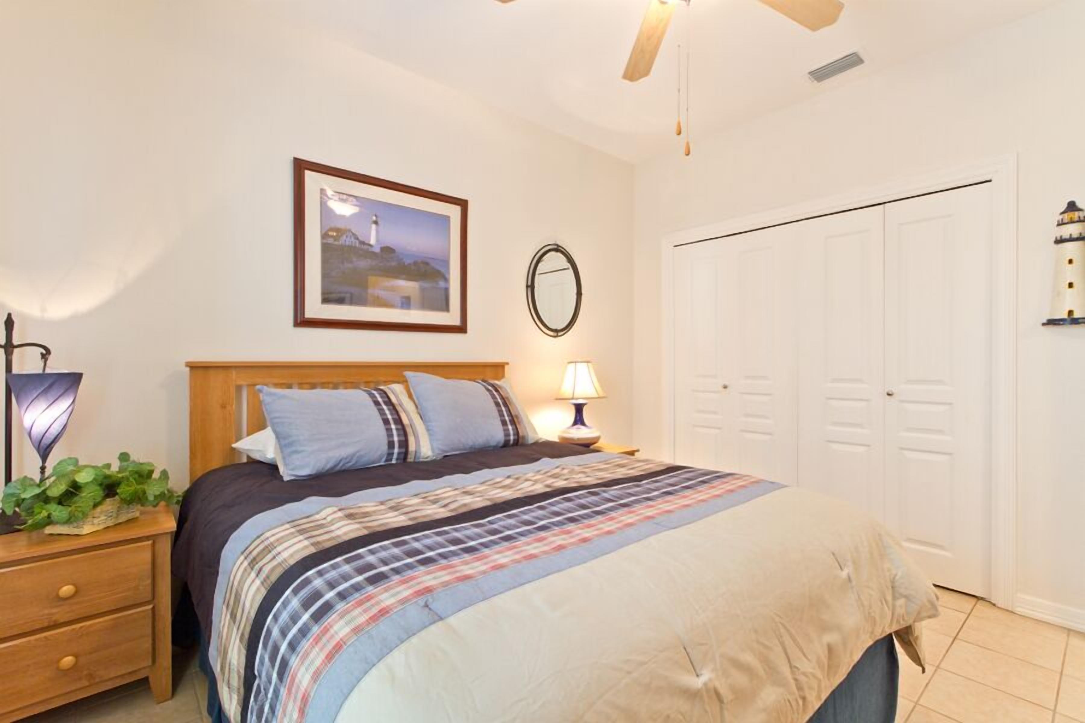 A bedroom with a bed, bedside table, lamp, and a framed picture on the wall.