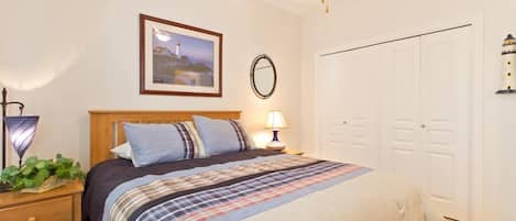 A bedroom with a bed, bedside table, lamp, and a framed picture on the wall.