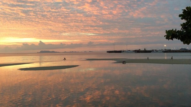 A waterfront scene with calm waters reflecting the sky, a pier with boats, and distant landforms. - Sri Samui Hotel (Koh Samui)