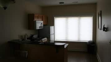 A kitchen with wooden cabinets, a microwave, a refrigerator, and a window with blinds.