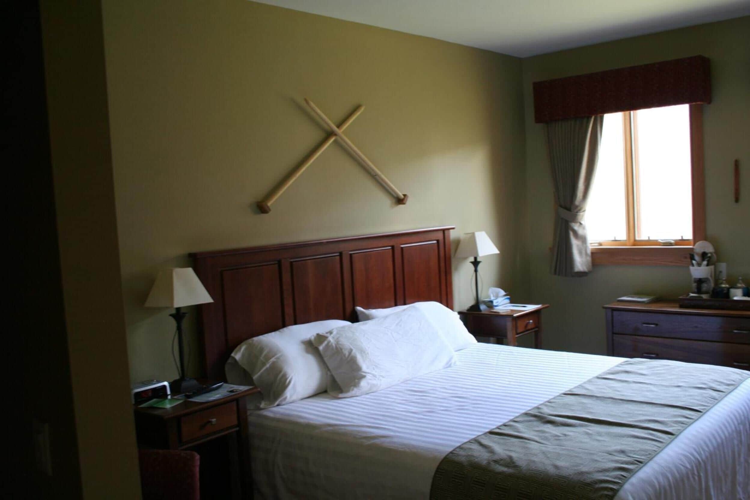 A hotel room with a wooden headboard, a bed with white linens, a nightstand with a lamp, and a window with curtains.