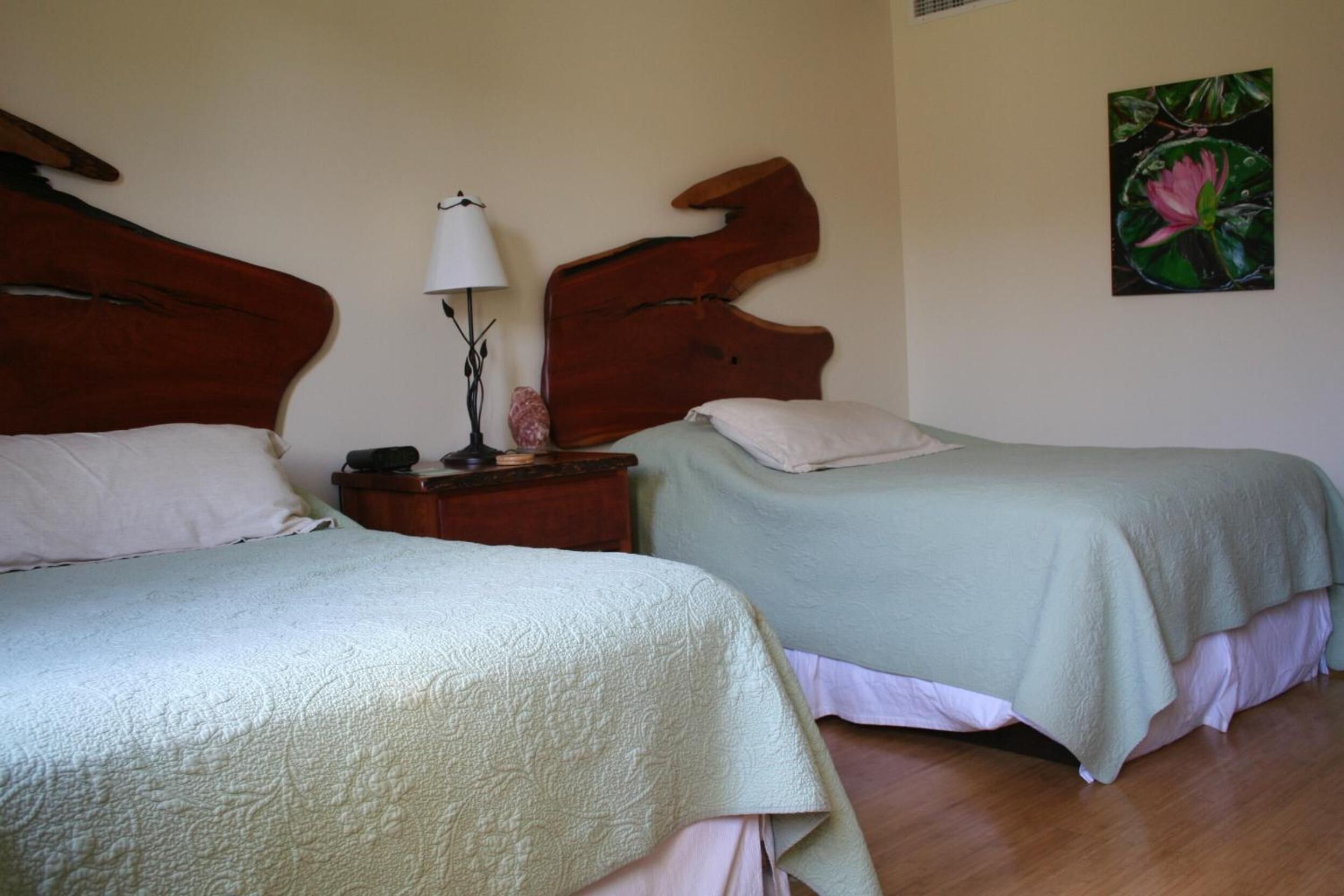 A room with two beds, a nightstand with a lamp, and a painting on the wall.