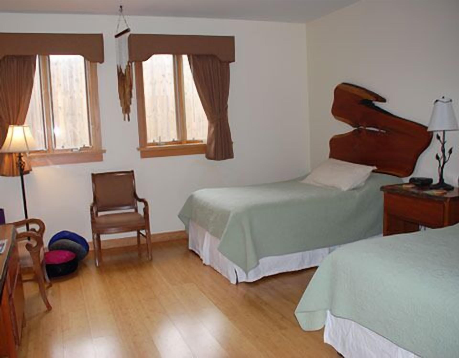 A room with two beds, a chair, a desk, and a lamp.