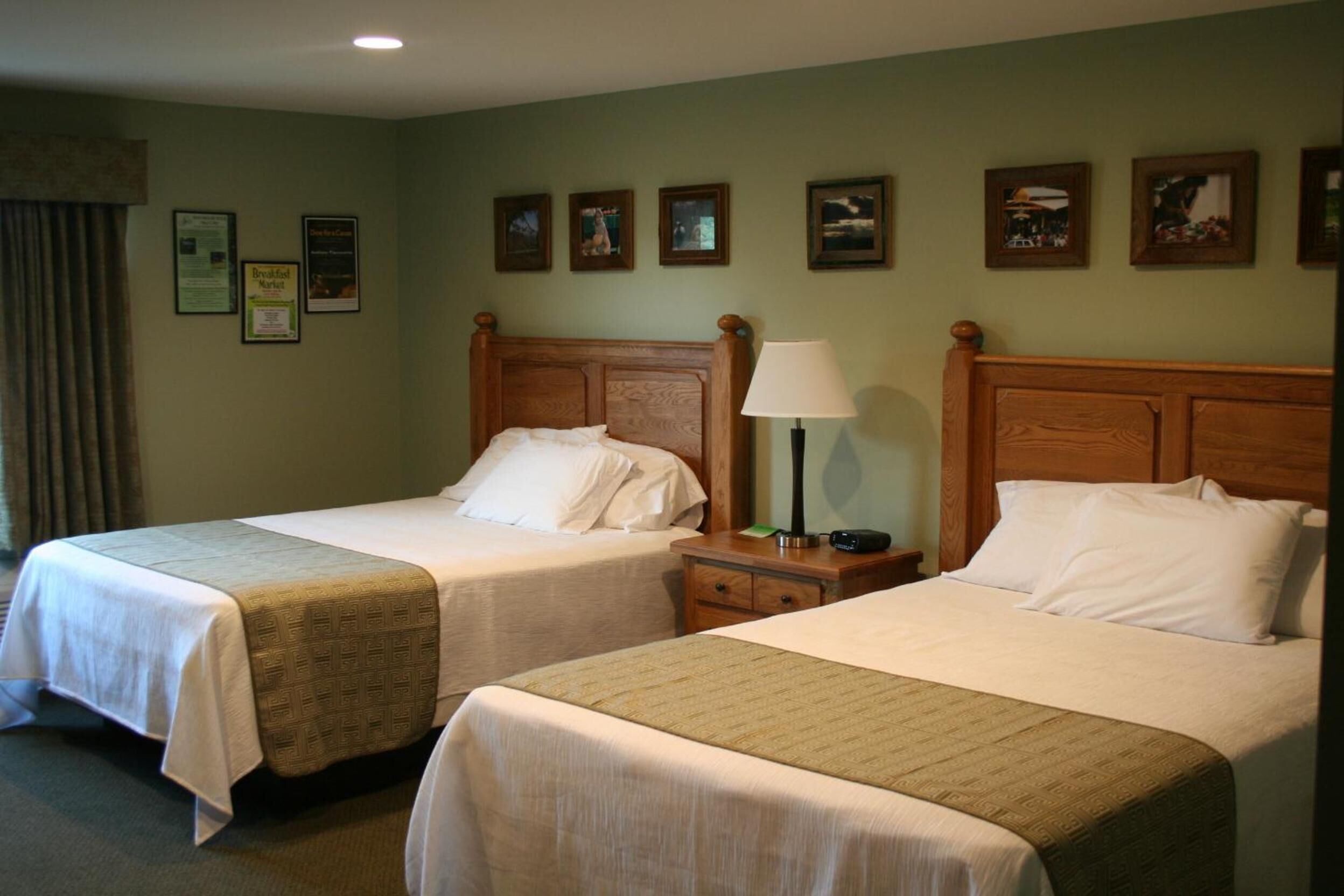 A hotel room with two beds, a nightstand with a lamp, and several framed pictures on the wall.