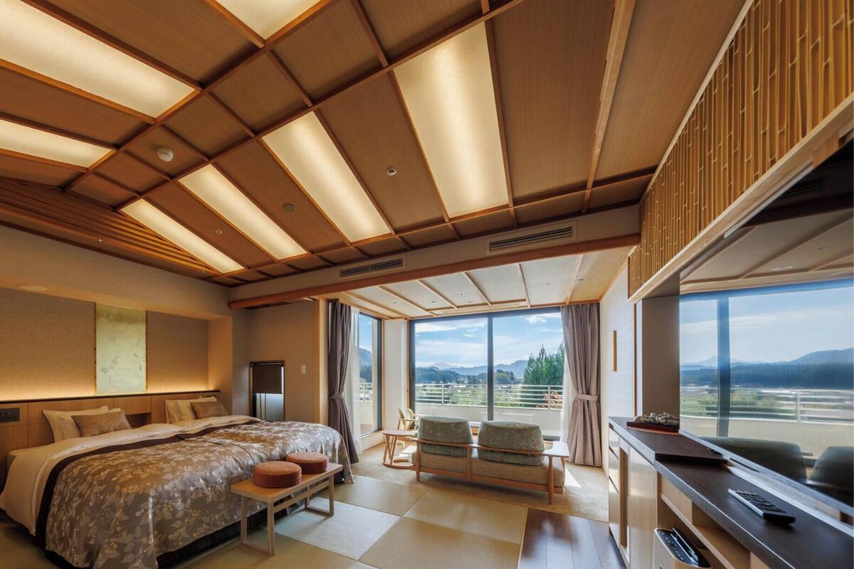 A modern hotel room with a large bed, a desk, a chair, and a balcony with a view of the mountains.