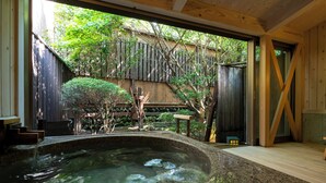 A spa area with a hot tub, wooden deck, and a view of a garden with a wooden fence and trees. - KINUGAWA GRAND HOTEL YUME no TOKI (Nikko)