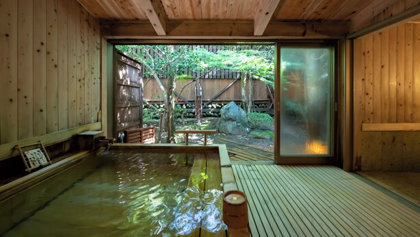 A traditional Japanese onsen with wooden interiors, a wooden deck, and a view of a garden with a wooden fence and trees. - KINUGAWA GRAND HOTEL YUME no TOKI (Nikko)