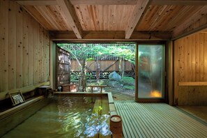 Uma onsen japonesa tradicional com interiores em madeira, um deck de madeira e vista para um jardim com cerca de madeira e árvores.