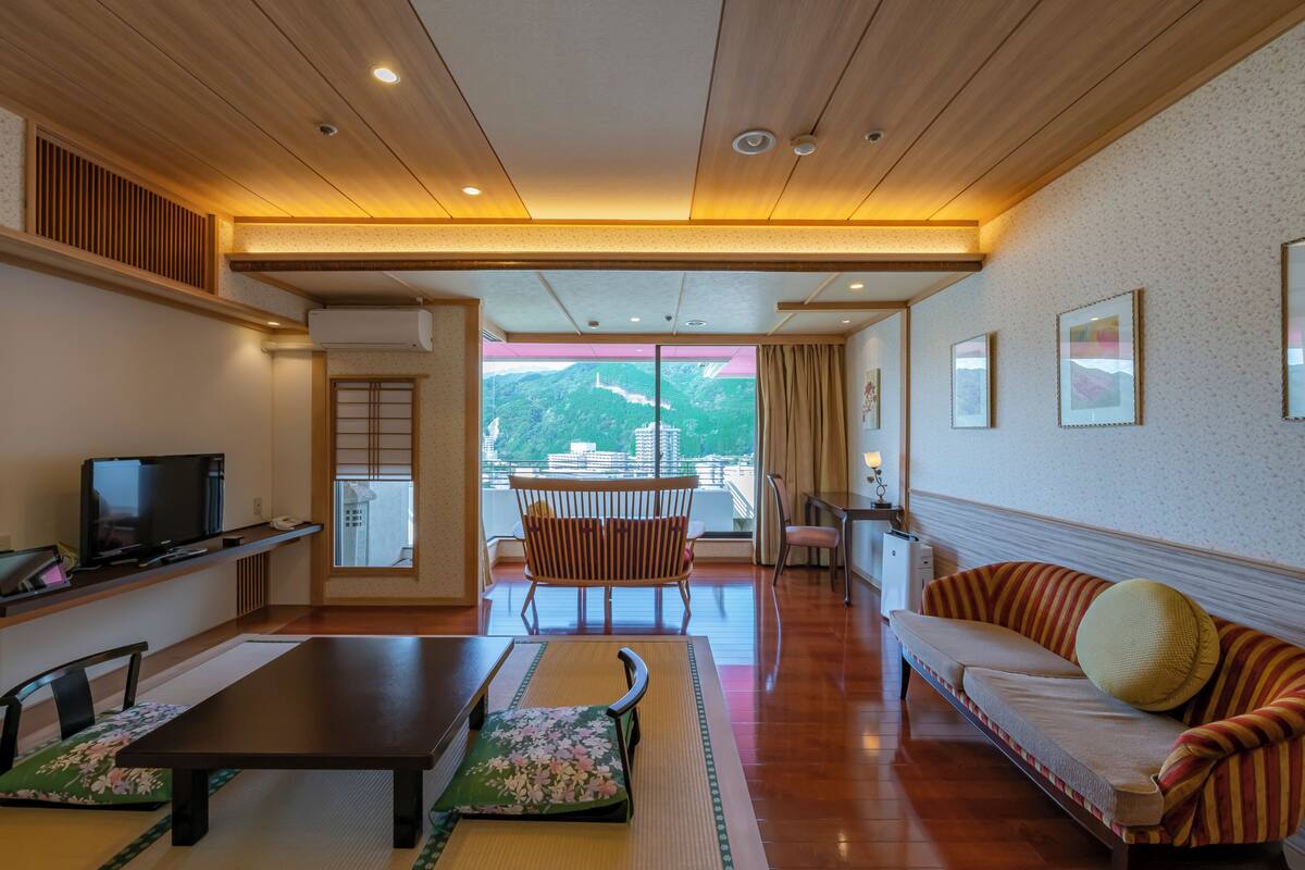 A traditional Japanese-style room with tatami flooring, a low wooden table, a sofa, and a television.