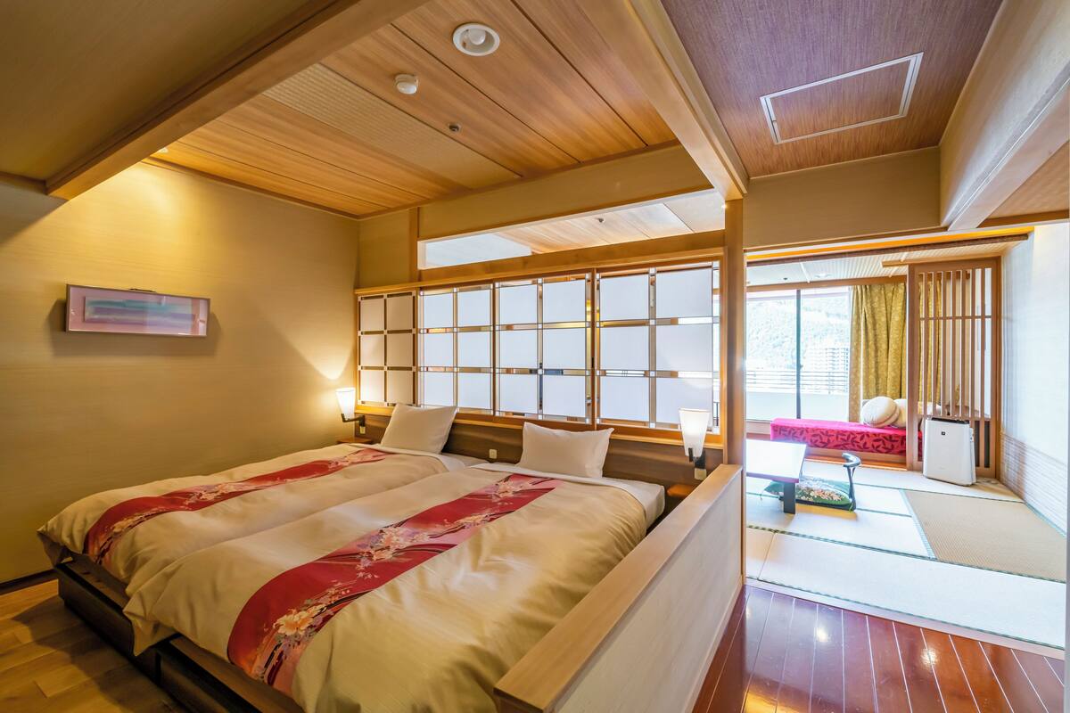 A traditional Japanese-style bedroom with a large bed, sliding shoji doors, tatami flooring, and a view of the outside.