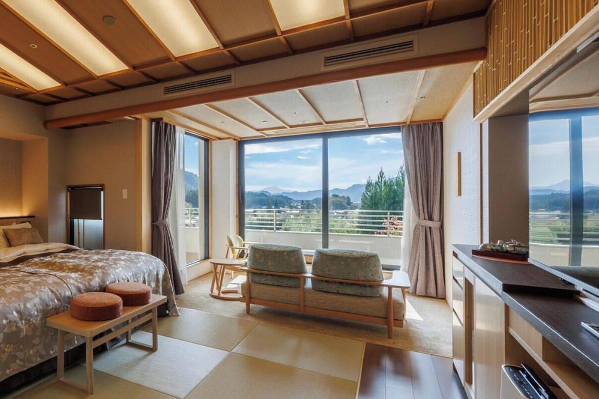 A modern hotel room with a large bed, a desk, and a balcony with a city view.