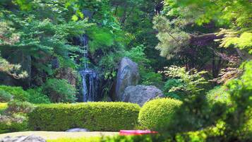A lush garden with a waterfall, neatly trimmed hedges, and large rocks.