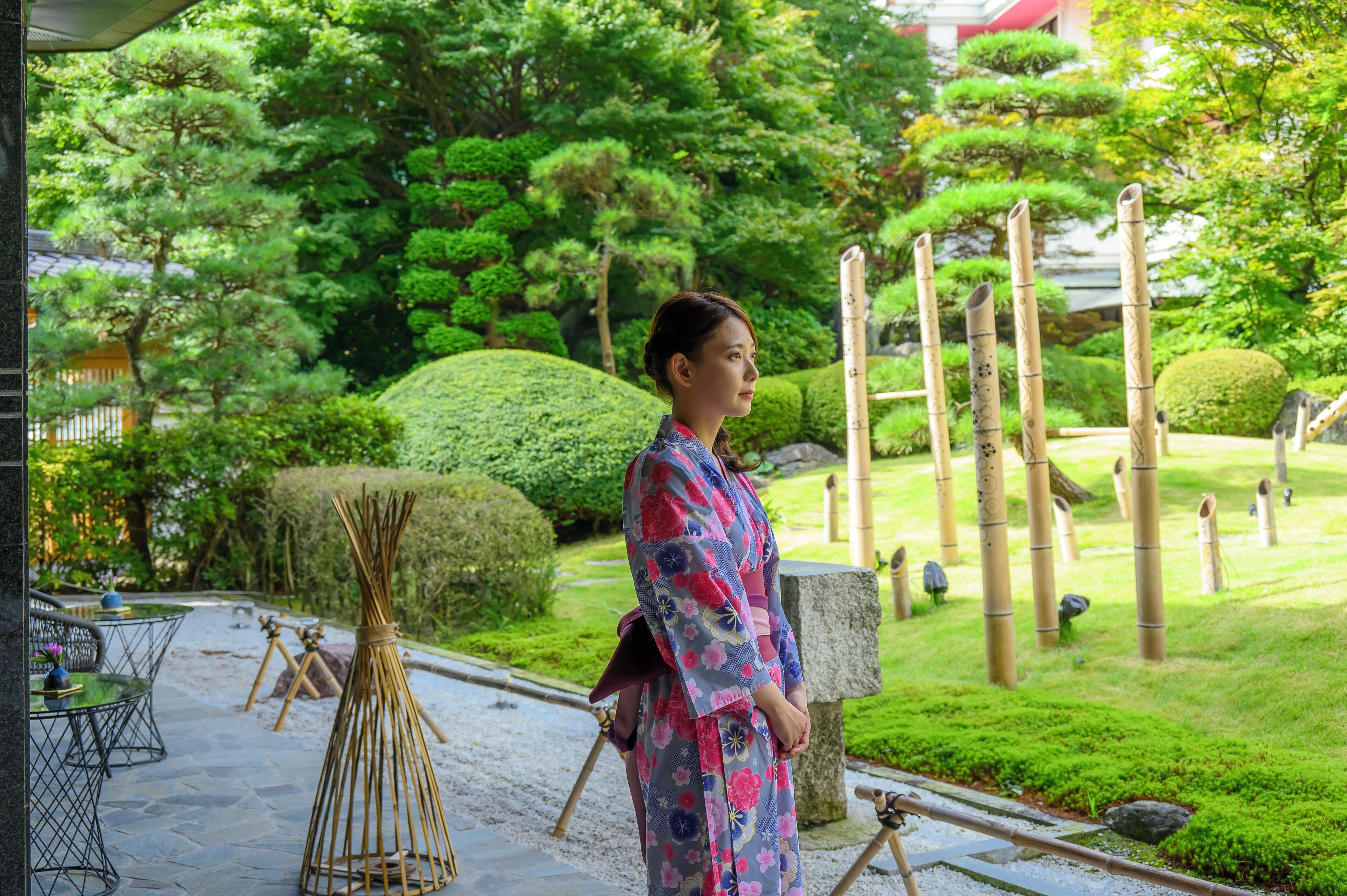 A traditional Japanese garden with a woman in a kimono, stone lanterns, and neatly trimmed bushes.