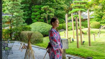 A traditional Japanese garden with a woman in a kimono, stone lanterns, and neatly trimmed bushes.