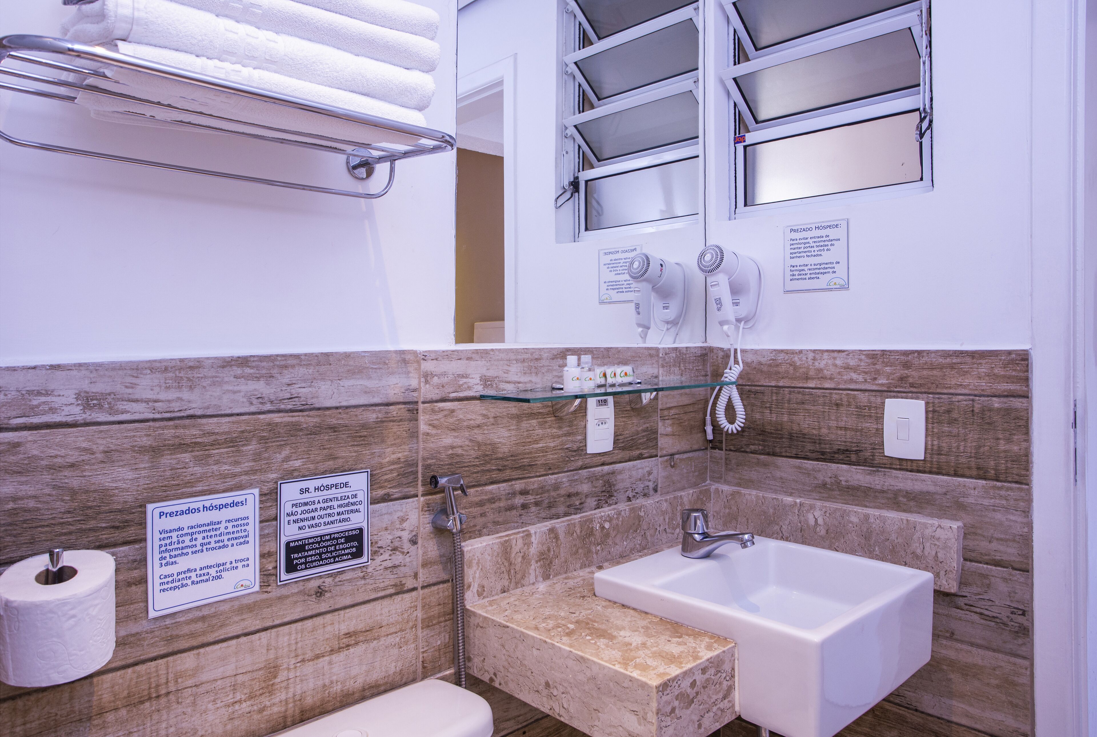 A bathroom with a wooden wall, a glass shelf, a sink, and a toilet.
