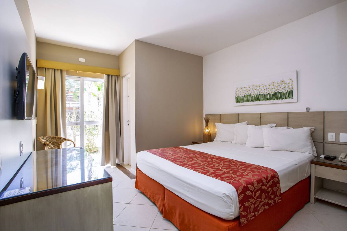 A hotel room with a bed, a desk, a chair, a TV, and a window with curtains.