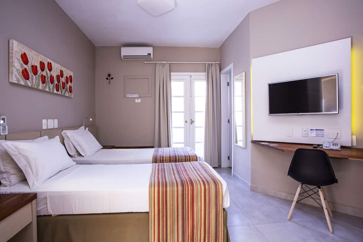 A hotel room with two beds, a desk with a chair, a TV, and a painting on the wall.