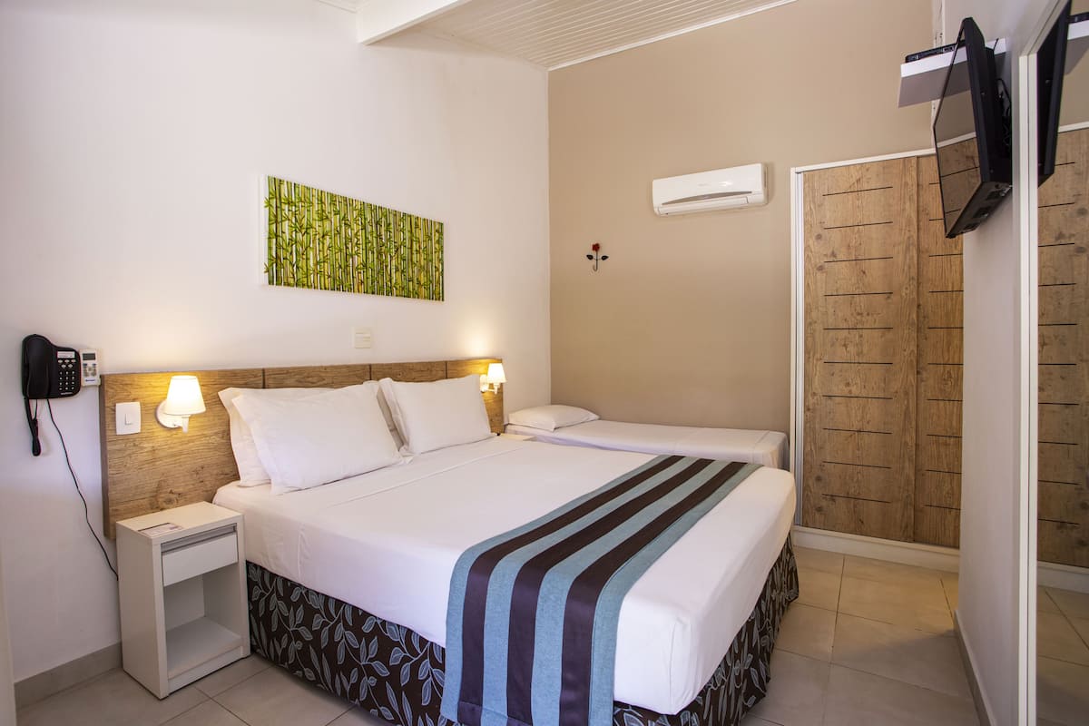 A hotel room with a bed, bedside tables, a wall-mounted air conditioner, and a wooden wardrobe.