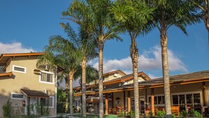 A two-story house with a covered patio, palm trees, and a well-maintained lawn. - Ciribaí Praia Hotel (São Sebastião)