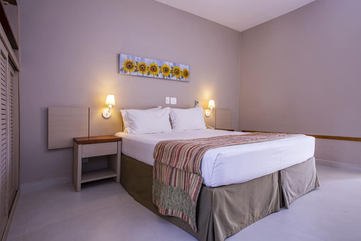 A bedroom with a bed, nightstands, a wall-mounted painting, and two wall-mounted lamps.