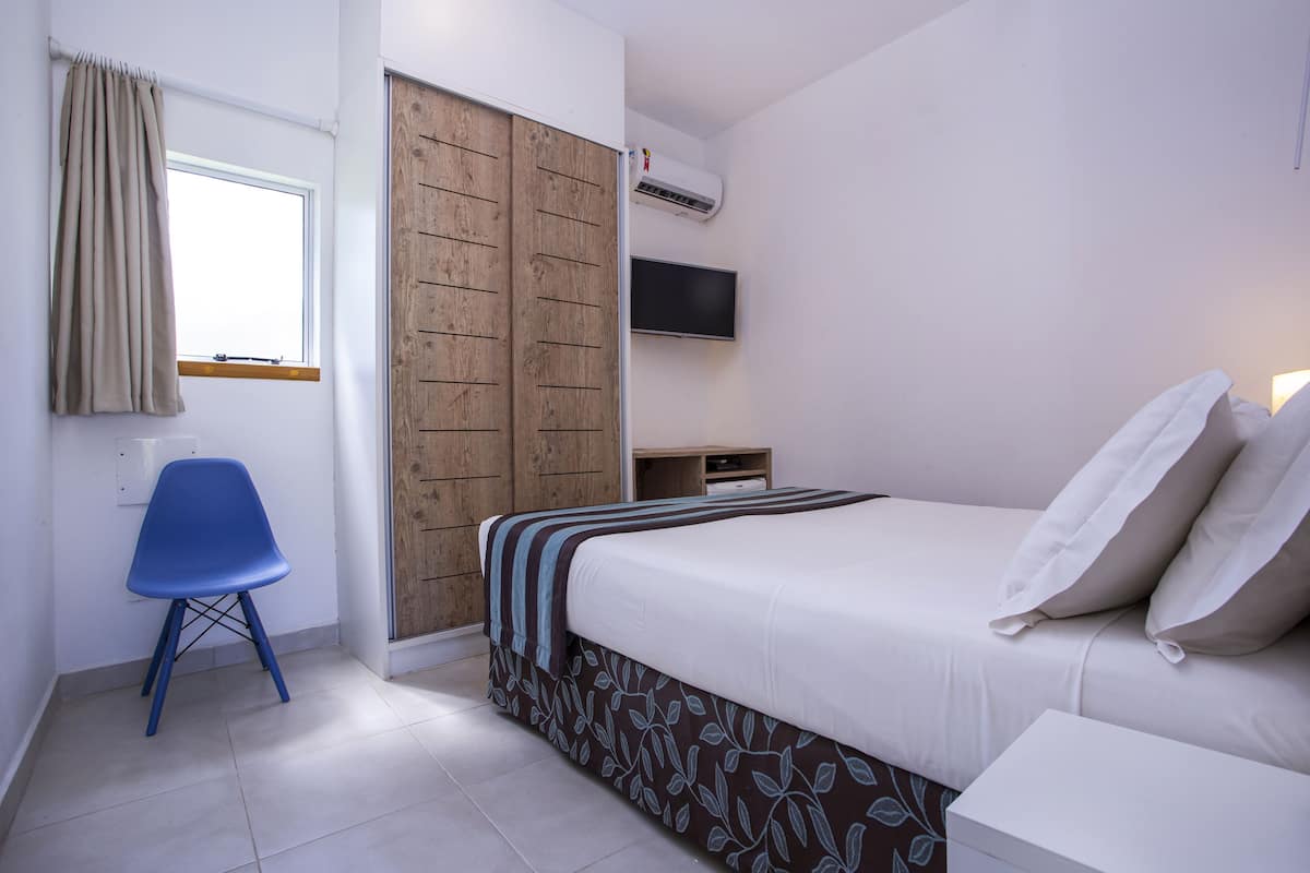 A bedroom with a bed, a TV, a wardrobe, and a chair.
