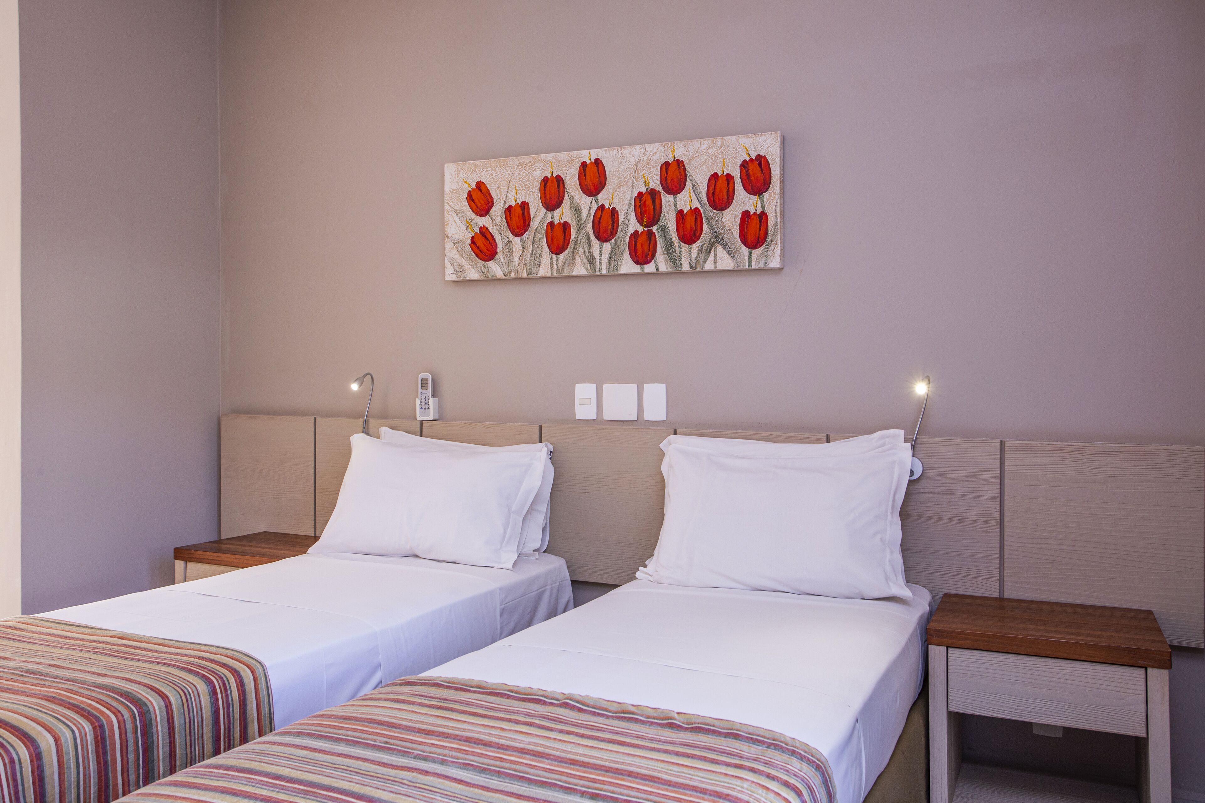 Een hotelkamer met twee bedden, een nachtkastje, een wandlamp en een schilderij van rode tulpen.