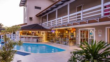 A hotel with a swimming pool, outdoor bar, and multiple dining areas.