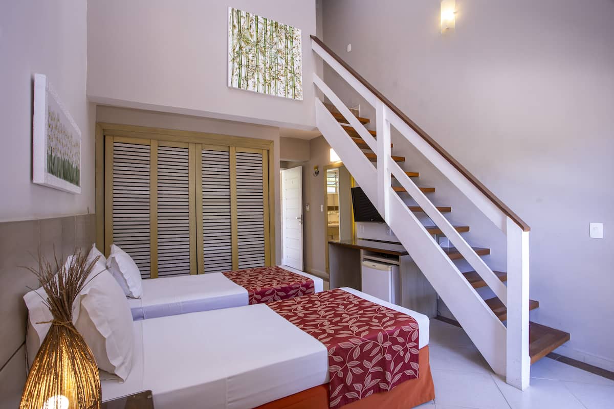 A bedroom with two beds, a staircase, and a view of a kitchen.