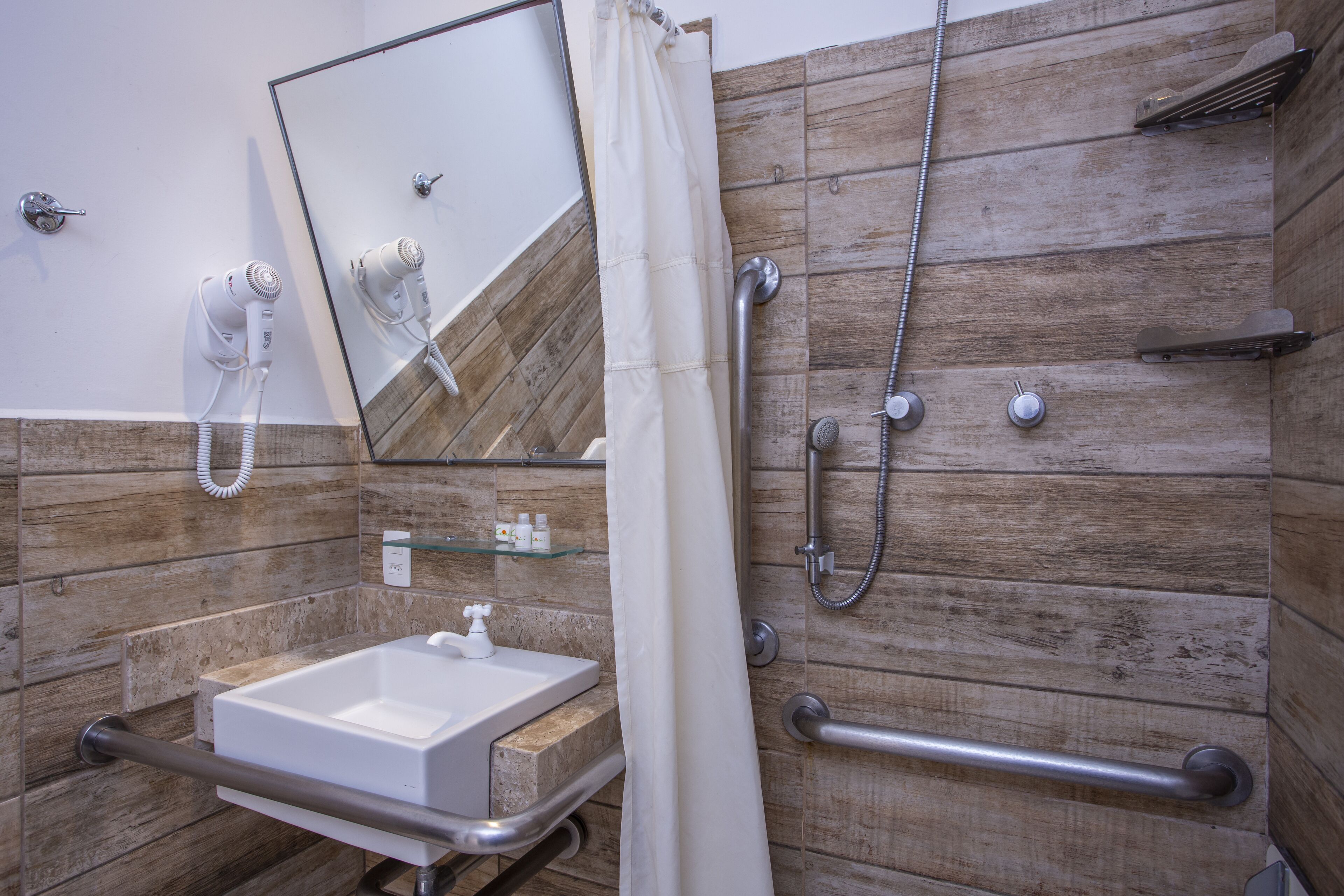 Une salle de bain avec un mur en bois, un lavabo, un miroir, une douche et une barre d’appui.