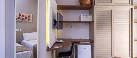 Een knus hotelkamer met een bed, een bureau met computer, een kleine koelkast, een stoel en een spiegel.