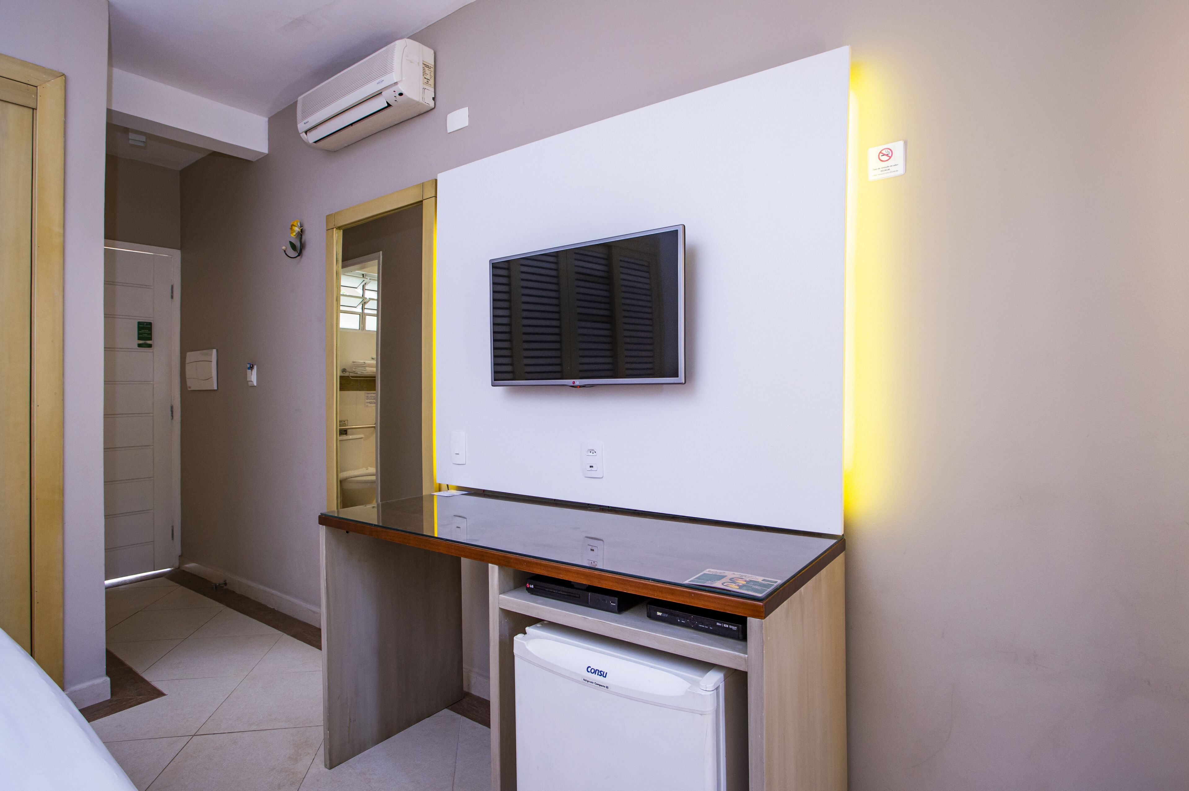 A compact hotel room with a kitchenette, a flat-screen TV mounted on the wall, and a small refrigerator.