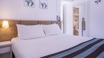 Quarto de hotel com cama, mesa de cabeceira, luminária na parede e duas obras de arte emolduradas.