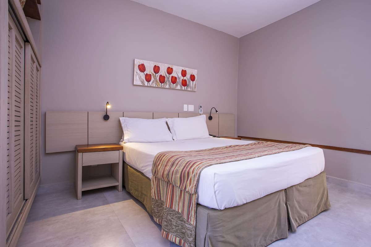 A bedroom with a bed, bedside tables, a wall-mounted lamp, and a painting.