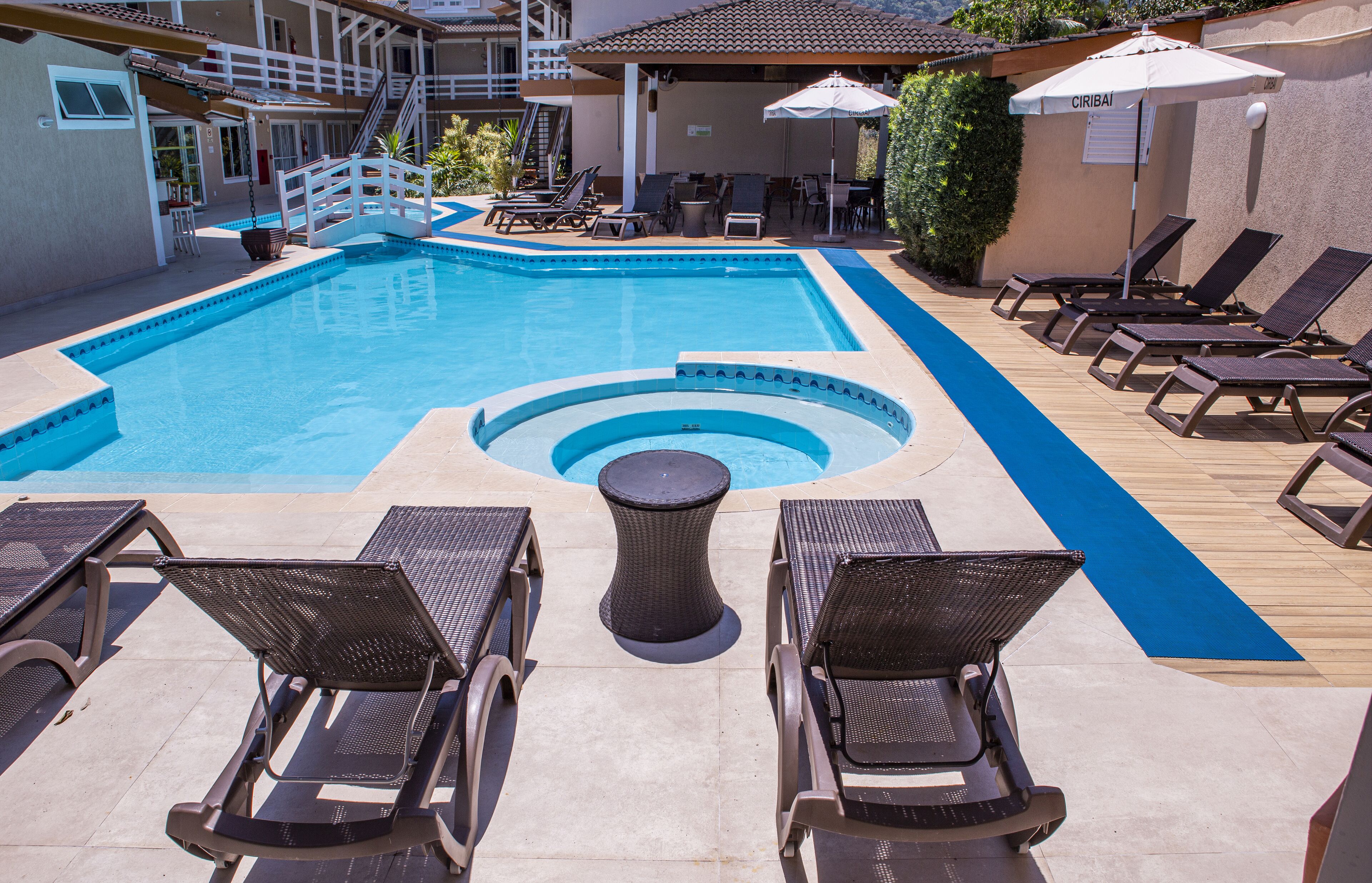 A swimming pool with lounge chairs and a small table, surrounded by a covered seating area.
