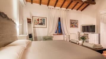 Un dormitorio con una cama grande, un escritorio con computadora, un televisor y obras de arte en las paredes.