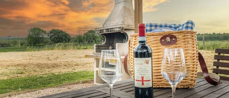 Una mesa de madera con una botella de vino, dos copas de vino y una cesta de mimbre con un mantel a cuadros.